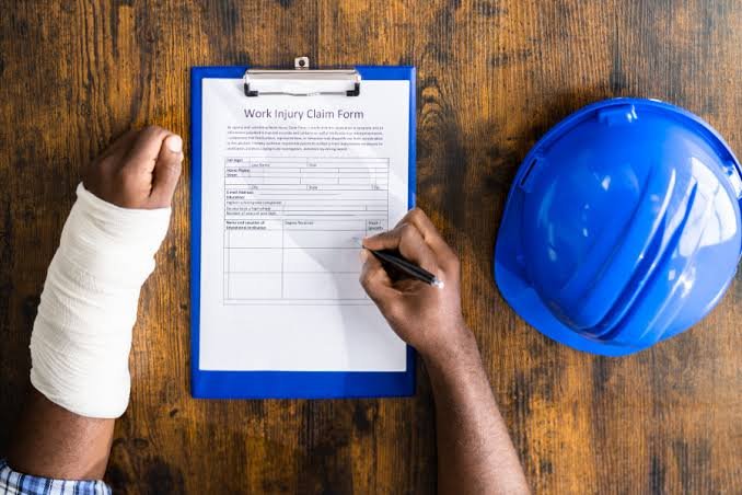 An injured worker with an arm cast filling out a work injury claim form next to a hard hat for an Injury Claim Attorney.