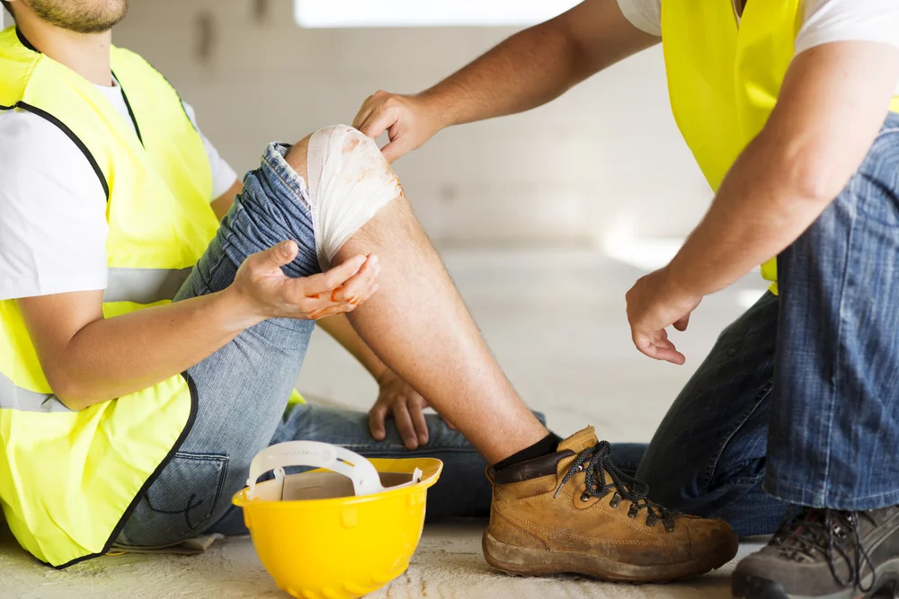 A worker applying a bandage to an injured colleague's knee at a construction site, representing Personal Injury Doral Florida legal services.