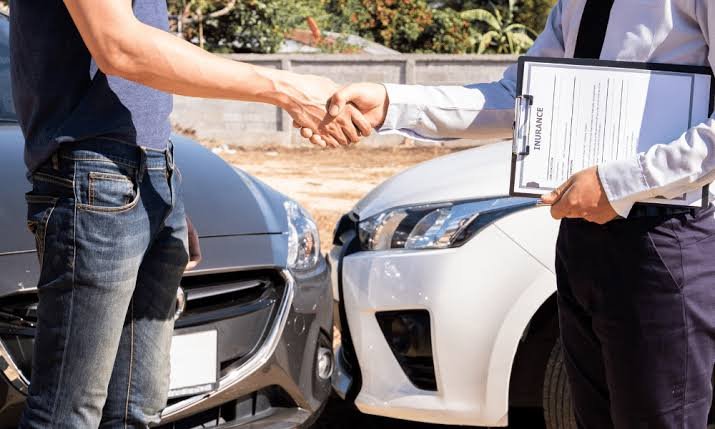Driver shaking hands with an insurance claims adjuster holding a clipboard between two collided vehicles, illustrating the settlement process supported by a Car Accident Claim Attorney.