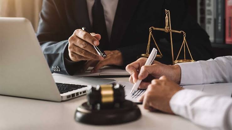 Client signing legal documents across a desk from a Personal Injury Claim Lawyer, with a laptop, gavel, and scales of justice in view.