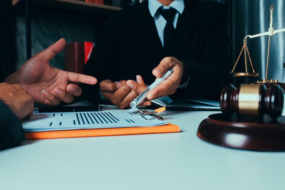 An attorney in a suit pointing a pen at legal documents on a clipboard during a consultation with a client, working as a Personal Injury Claim Lawyer beside a gavel and scales of justice