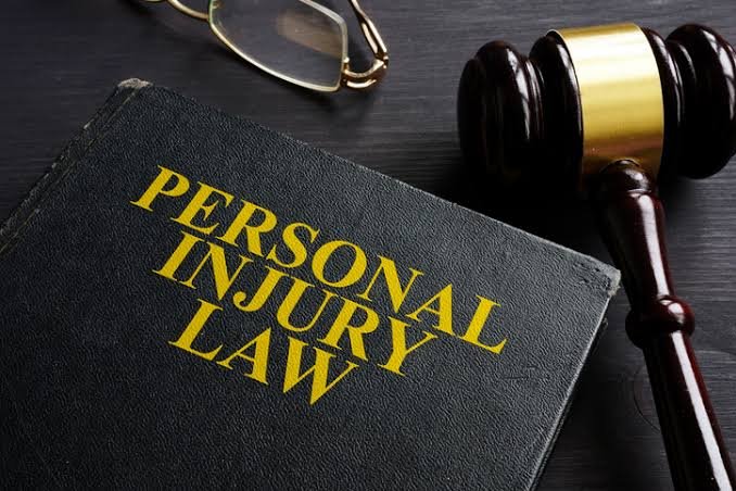 A legal book titled Personal Injury Law resting on a dark desk beside a wooden gavel and reading glasses, essential tools for a Personal Injury Claim Lawyer.