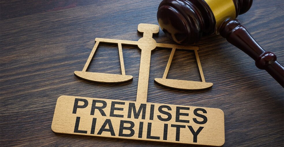 A wooden scales of justice cutout reading "PREMISES LIABILITY" placed next to a judge's gavel on a dark wooden surface, representing cases handled by a Premises Liability Injury Lawyer.