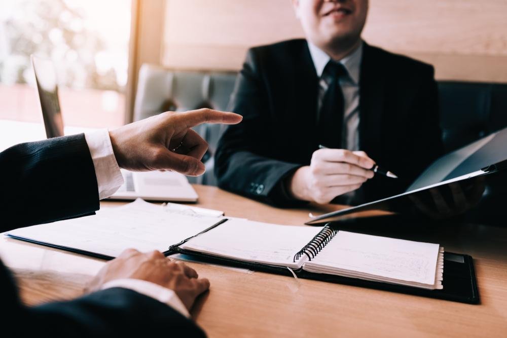 A client pointing to open documents while consulting with an attorney holding a notepad across a desk, demonstrating a consultation with a Premises Liability Injury Lawyer.
