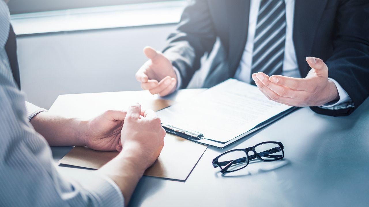 An attorney gesturing open-handed while explaining legal options to a client across a desk with paperwork and glasses, illustrating a strategy session with a Premises Liability Injury Lawyer.