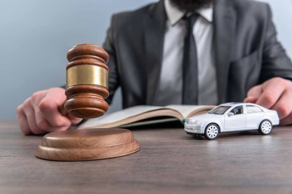 A lawyer in a suit holds a wooden gavel poised above its sounding block, with an open law book and a toy model car on the desk, symbolizing legal representation for victims of a Car Accident Hollywood Florida.