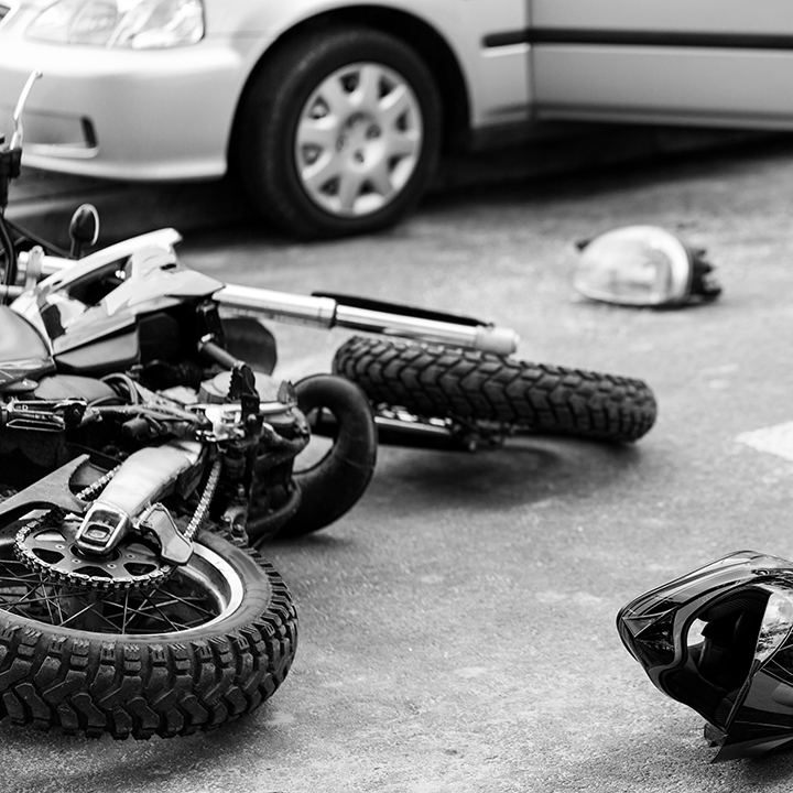 Aftermath of a serious Motorcycle Accident Miami Florida, featuring a wrecked motorbike on its side, a detached helmet on the asphalt, and a silver sedan with its door open on a rural road.