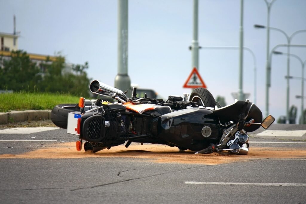 An after-accident scene following a Motorcycle Accident Miami Florida, showing a motorcycle lying on its side in an intersection, covered by a patch of oil-absorbent sand on the pavement, with traffic lights and a caution sign in the background.