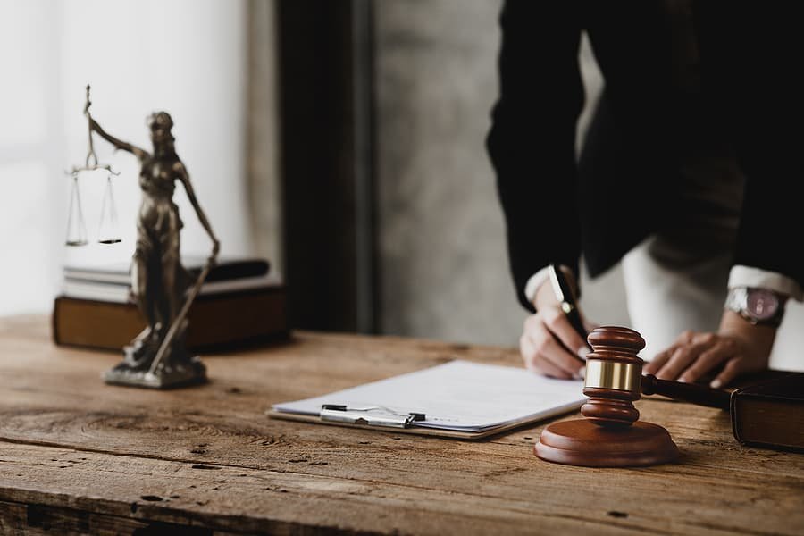 A lawyer signs a legal document at a rustic wooden desk featuring a gavel and a statue of Lady Justice, reflecting the meticulous document preparation standard for a dedicated Personal Injury Case Lawyer.