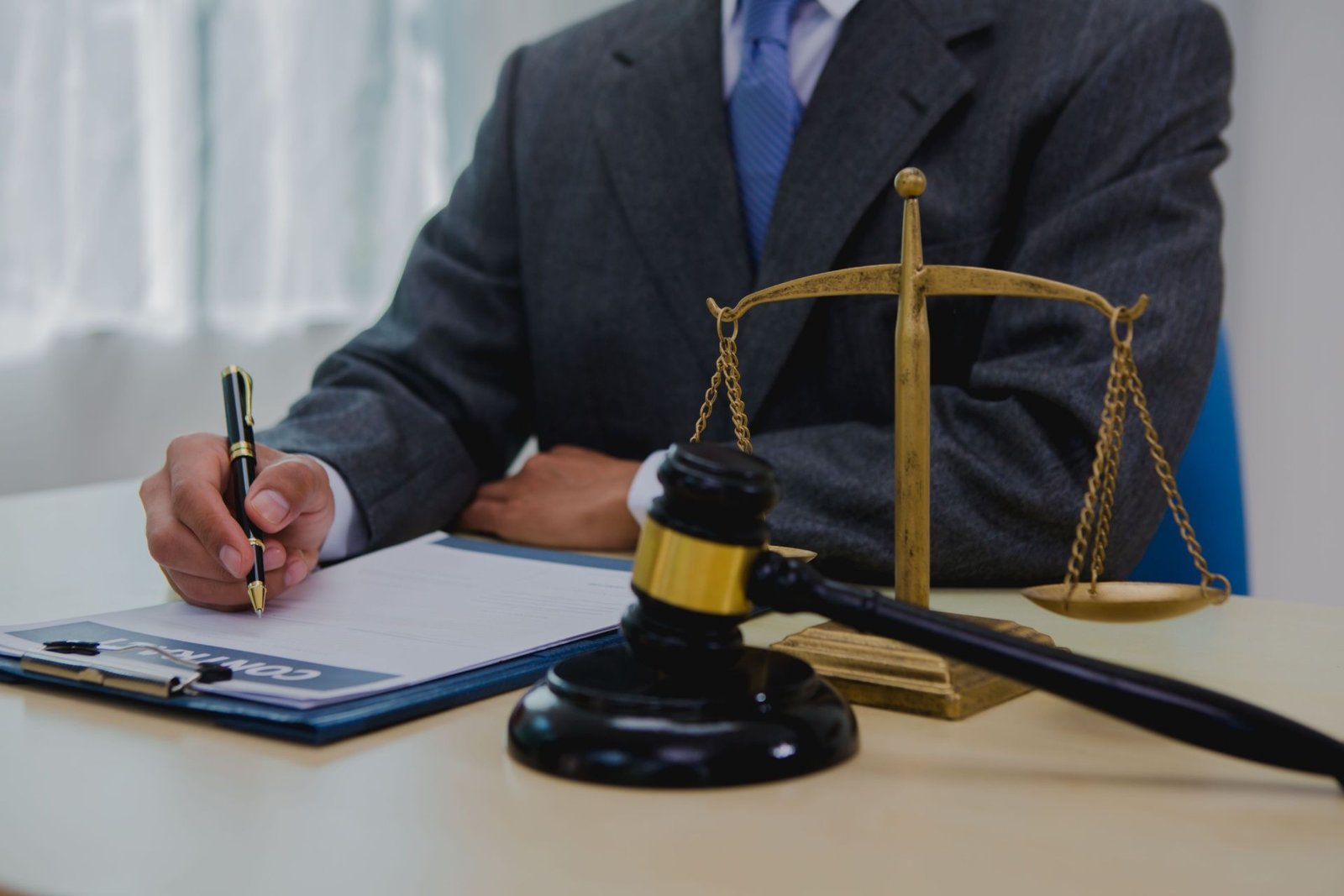 A professional in a suit and tie signs paperwork at a desk next to a wooden gavel and a brass scale of justice, representing the meticulous document handling required by an expert Personal Injury Case Lawyer.